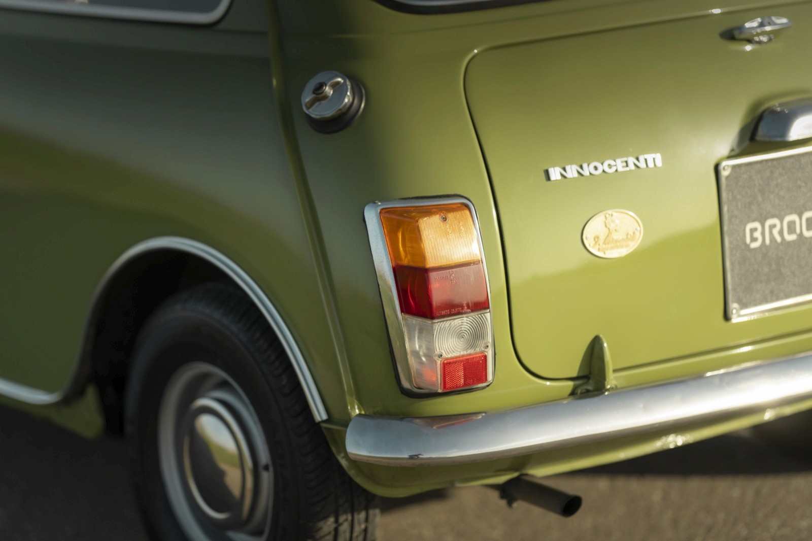 Close-up of the rear of a vintage green car, showcasing the tail light and part of the bumper.