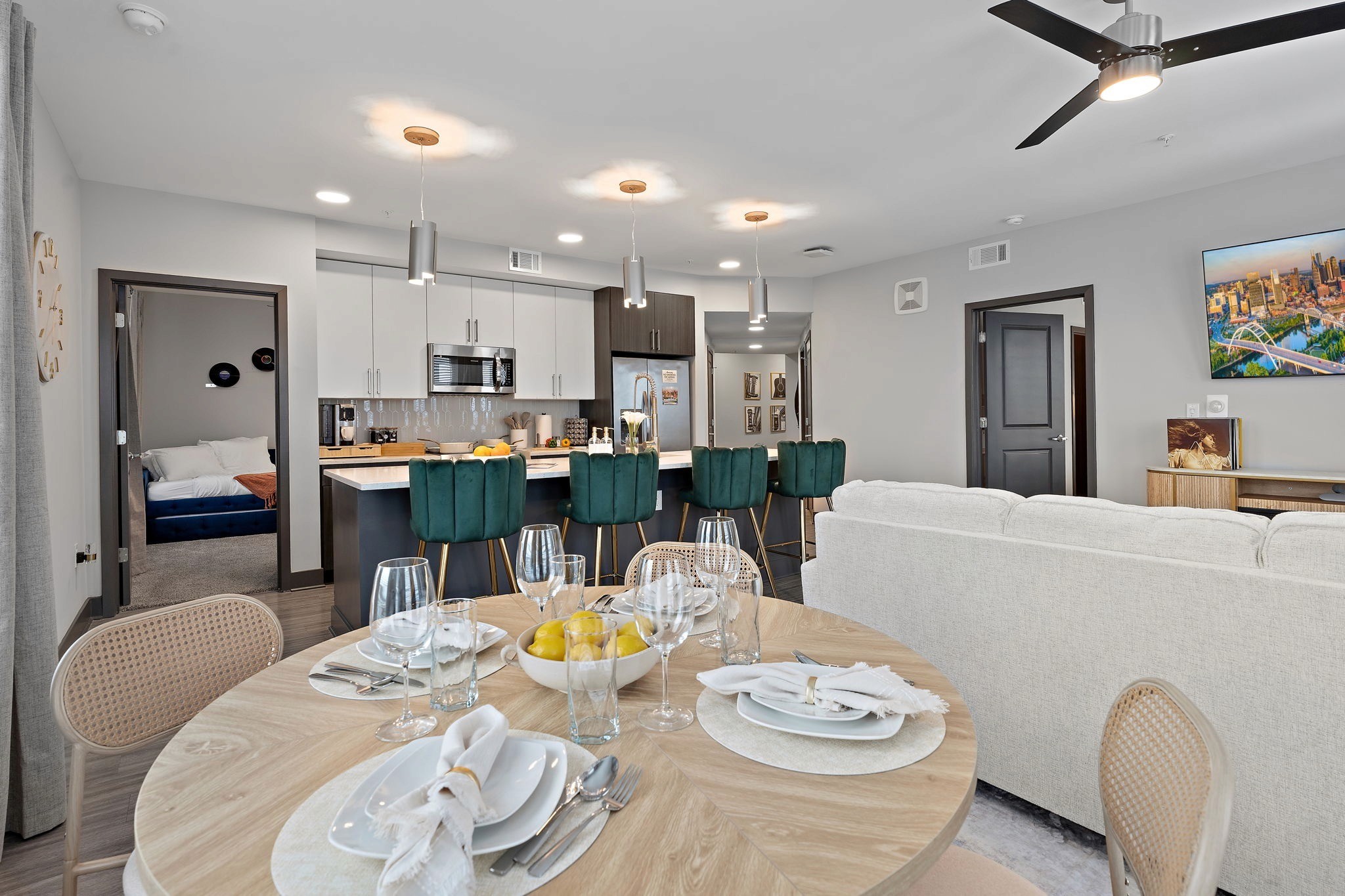 Open-concept living area with dining table, kitchen island, green barstools, and contemporary furnishings.