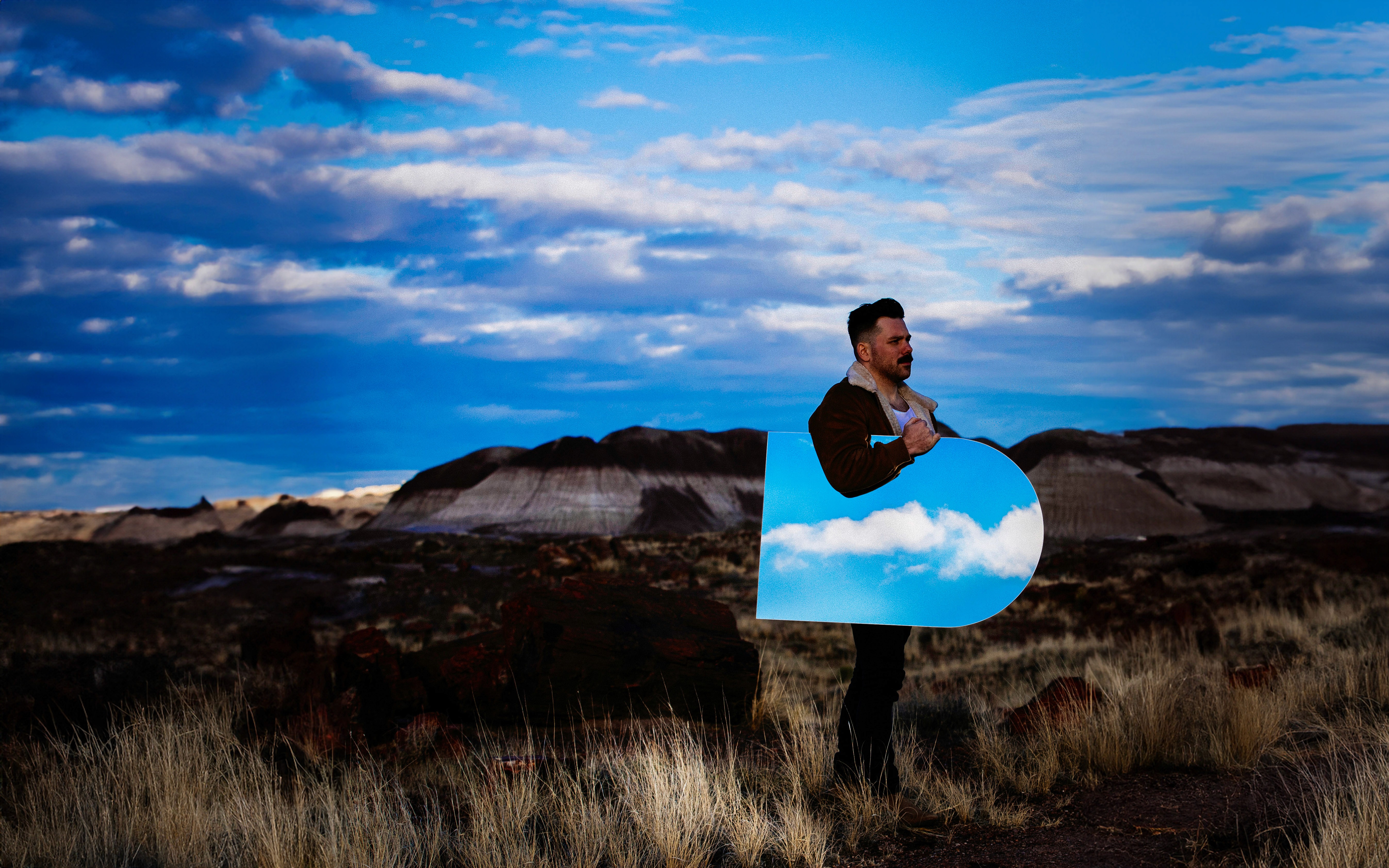 The lead singer of the band A R I Z O N A holding a tombstone made of mirrors while walking through Giant Logs Trail in Petrified Forest National Park