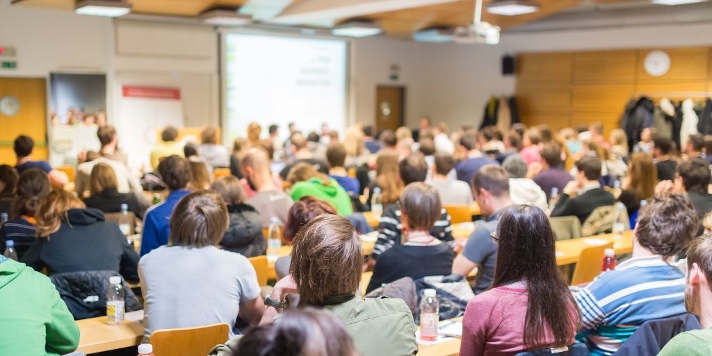 Aula universitaria piena durante seminario: formazione frontale con slide proiettate