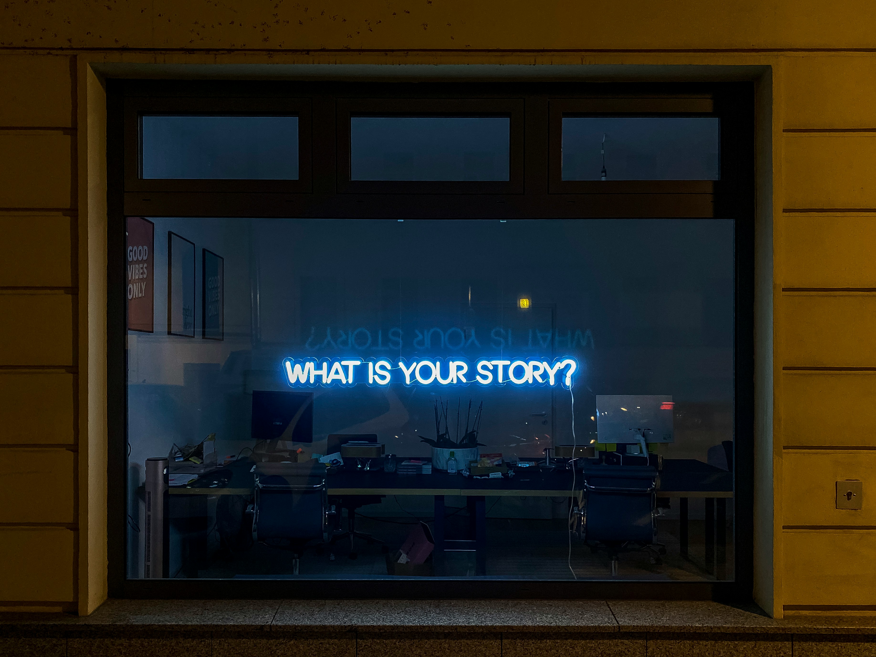 Frase motivazionale neon fotografata attraverso un vetro che chiede "qual'è la tua storia?"