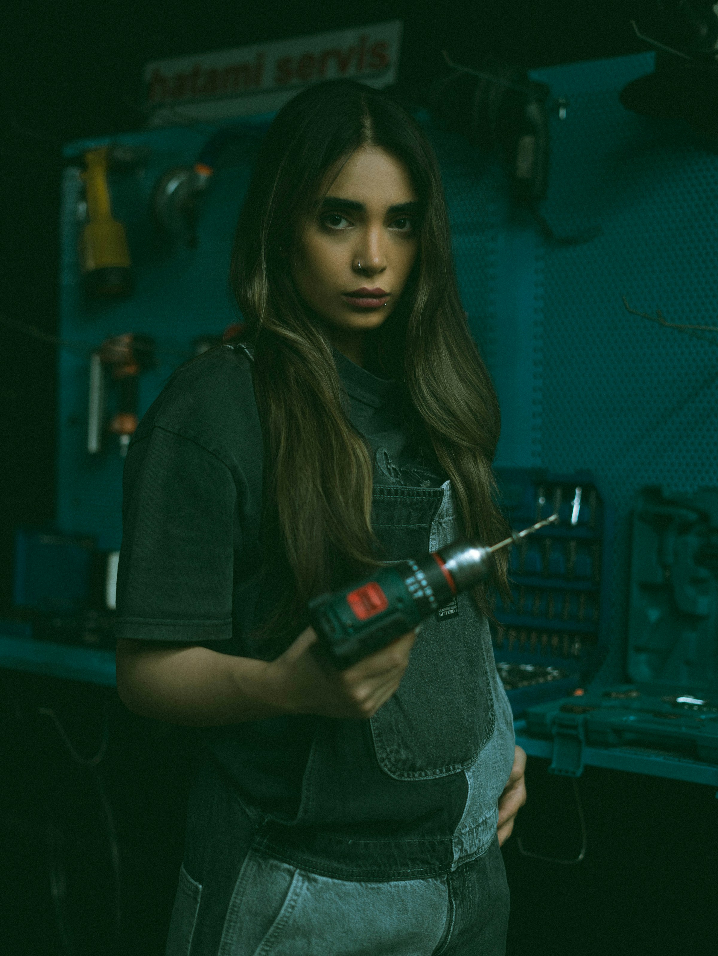 Portrait of a woman in work overalls holding a cordless drill in a workshop