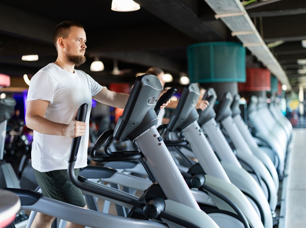 man at a line of machines at the gym using an elliptical for weight loss