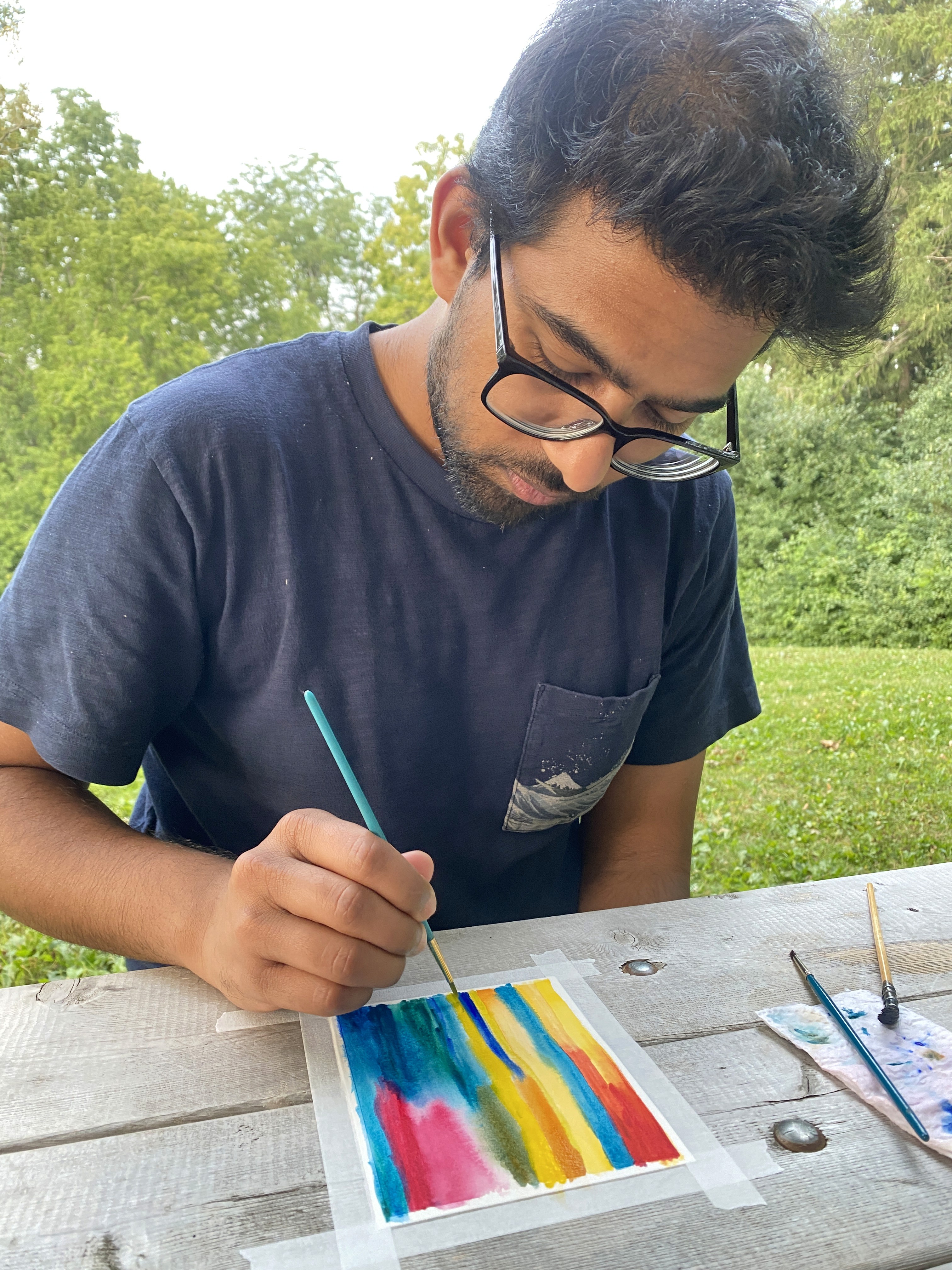 Rahul, co-founder and website designer at Visual Mess Studio — seated outdoors with a watercolor paper, specialising in Framer website design and brand strategy for creative small businesses