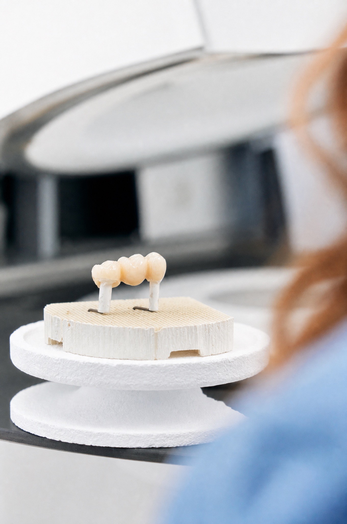 A close-up shot of a multi-unit ceramic dental bridge resting on a white firing tray inside an open dental sintering furnace.