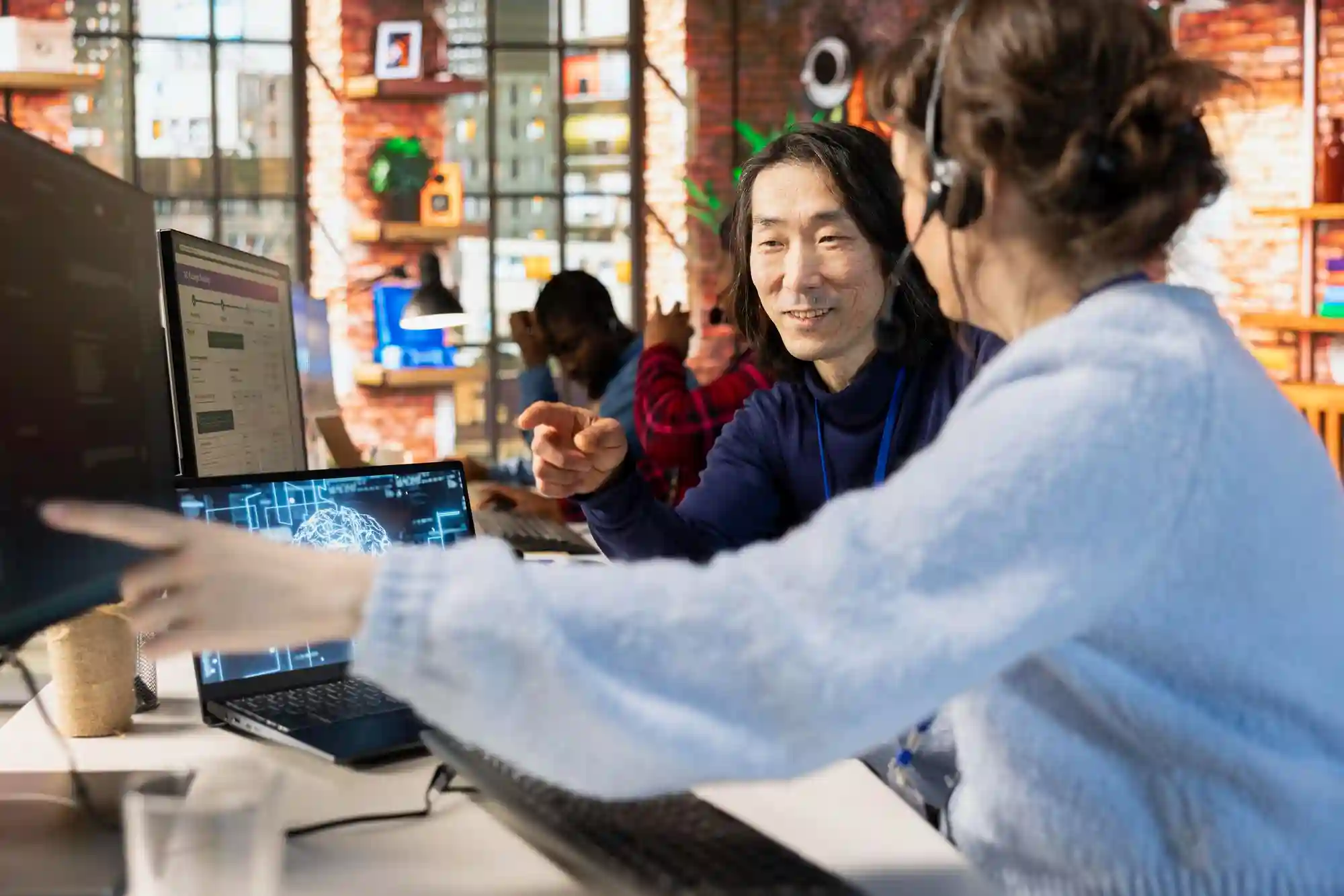 Two office colleagues collaborating on a digital project while looking at a computer monitor in a modern workspace.