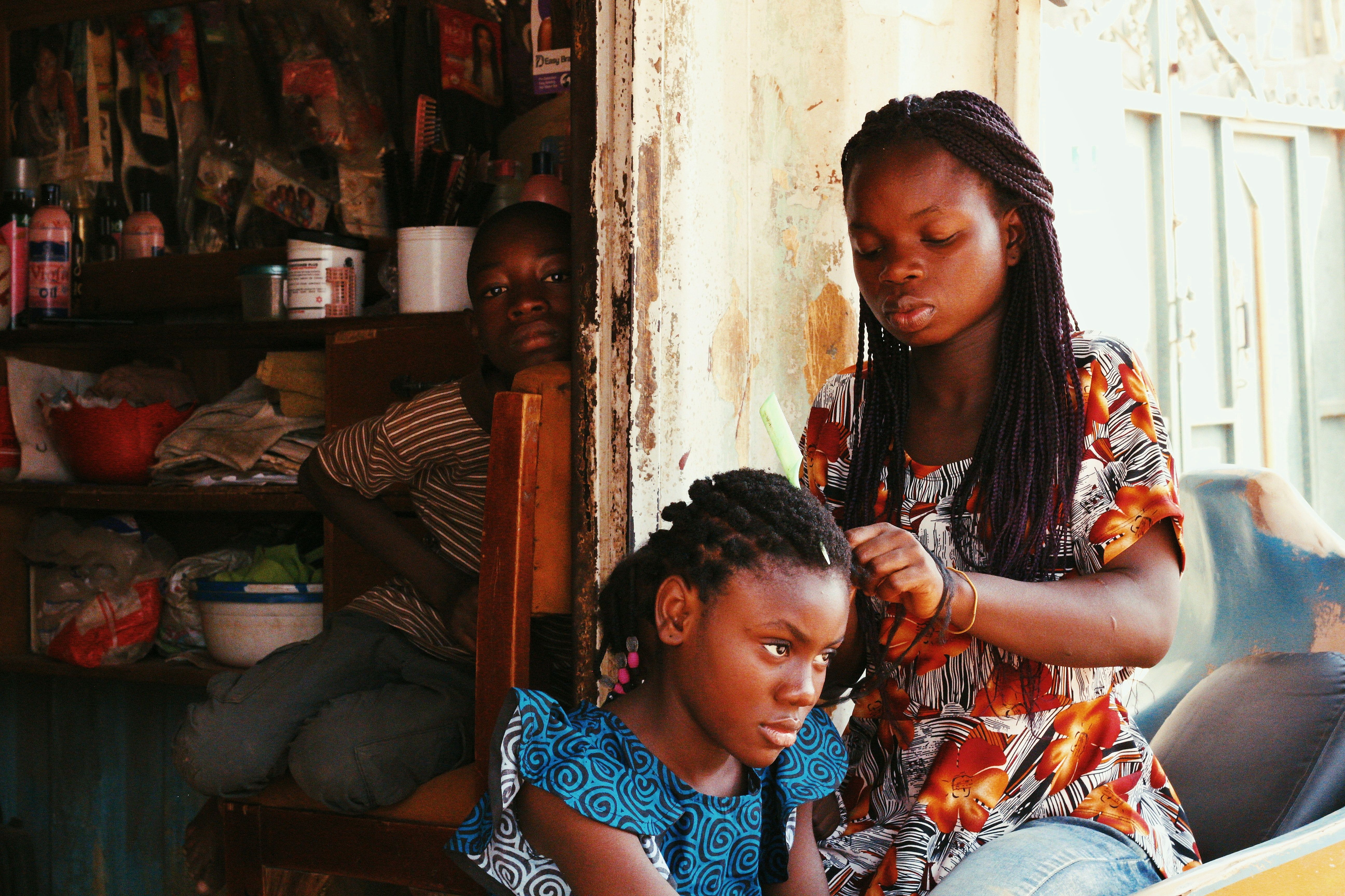 A young girl gets her hair braided by another girl in a small Nigerian shop..Muhammad-Taha Ibrahim.