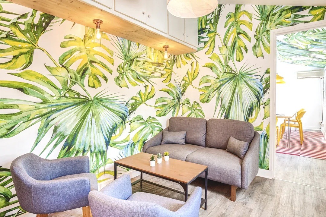 Espace lounge chaleureux avec papier peint à motif tropical, fauteuils confortables et ambiance conviviale.