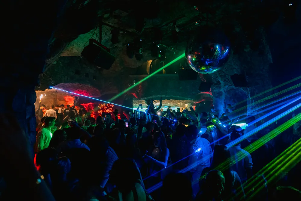 A cave nightclub in Positano with laser lights, a mirror ball and a crowd dancing.