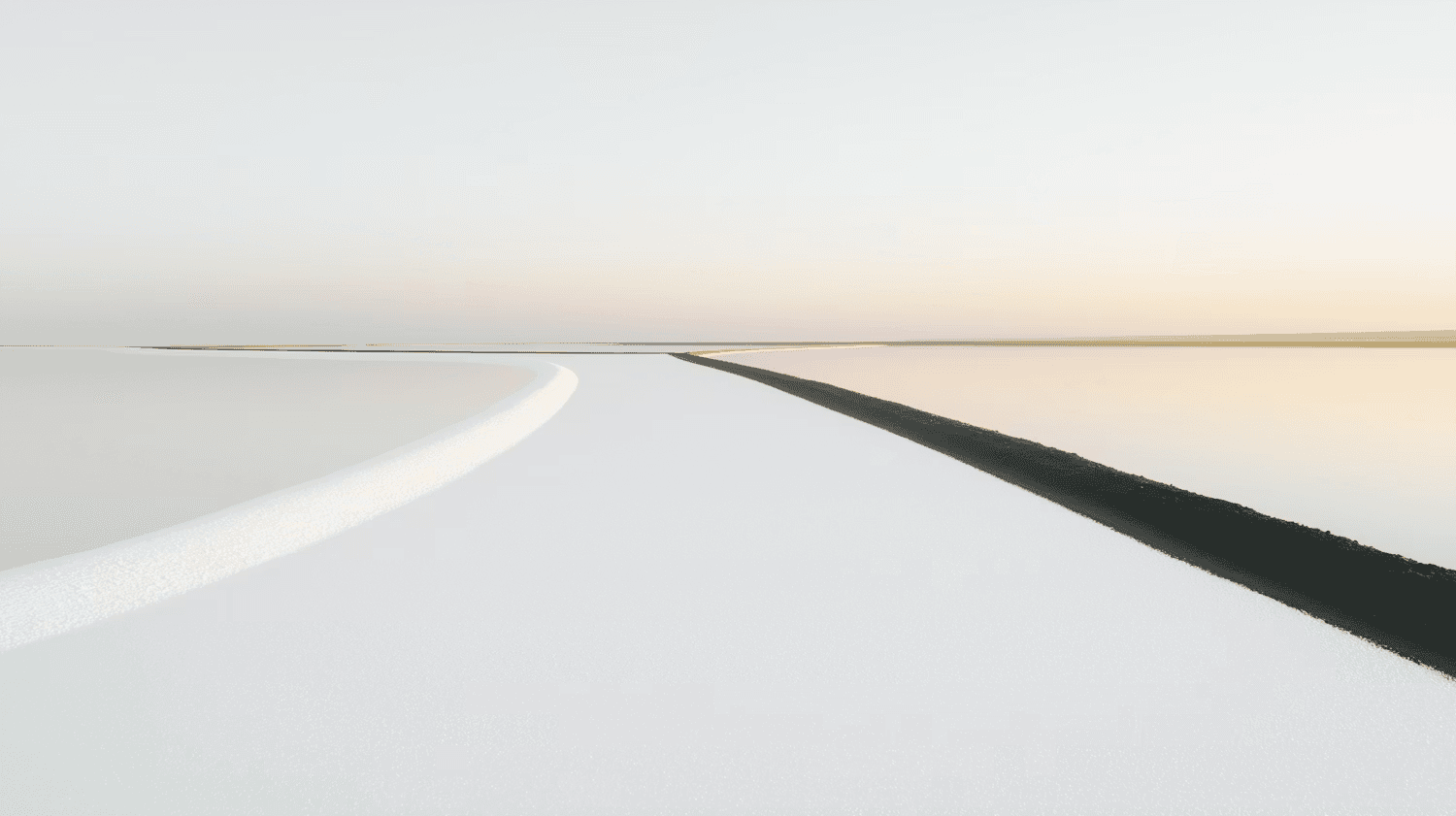 A straight asphalt road leading toward a distant horizon under a pale, sunset sky.