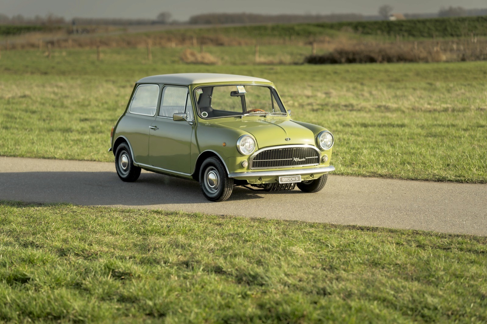 A vintage green car driving on a winding road through a grassy landscape under a clear sky.
