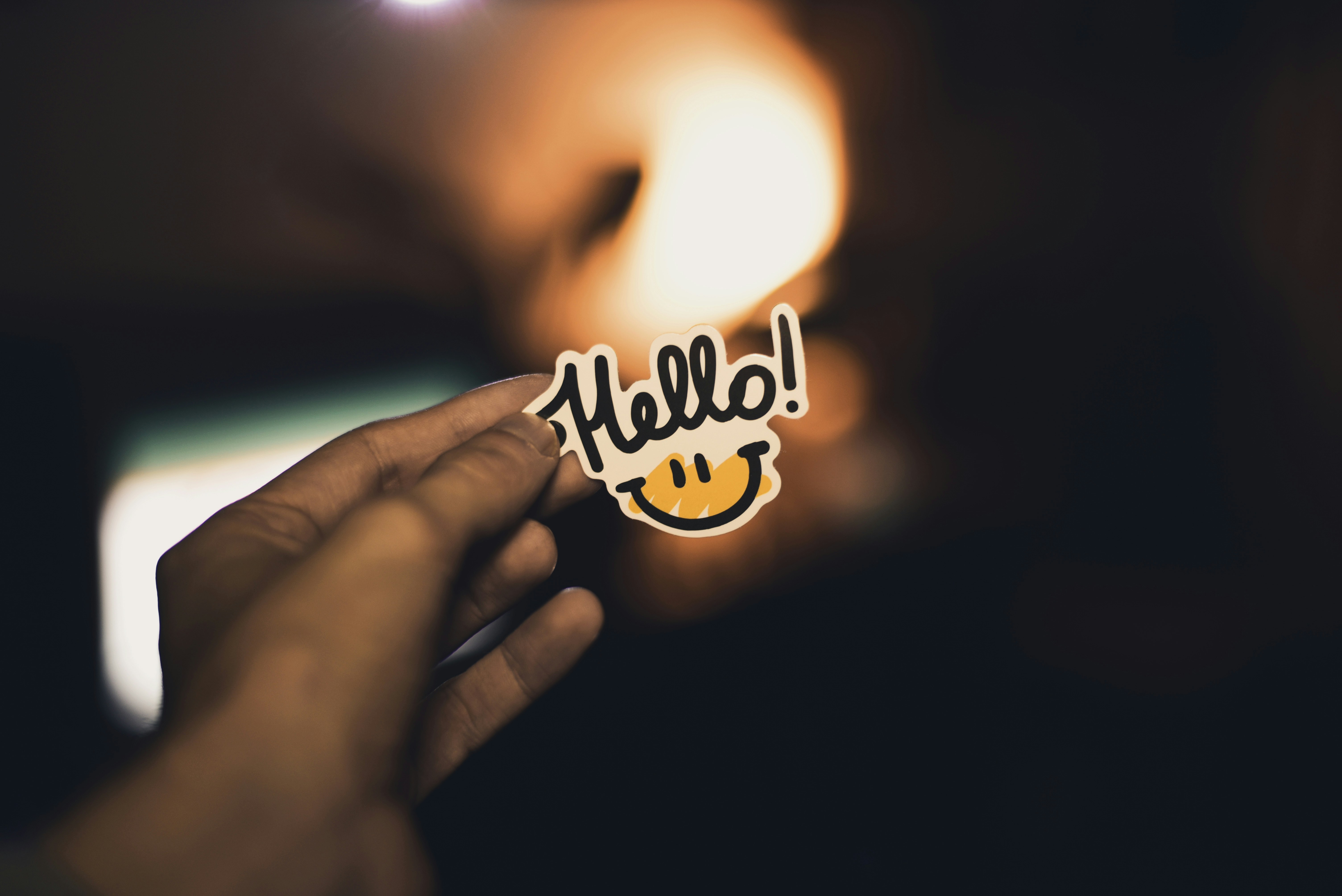 A hand holding a "Hello!" sticker with a smiley face