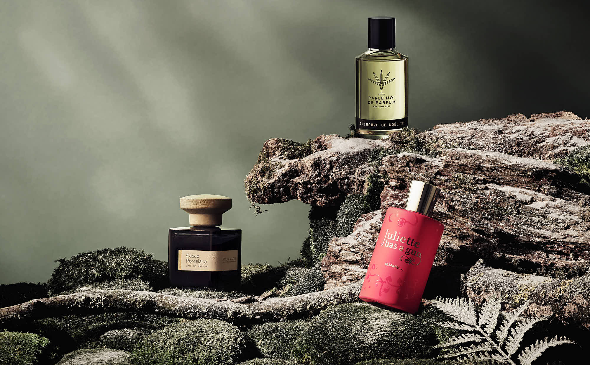 Luxury perfume bottles on mossy rock with green background.