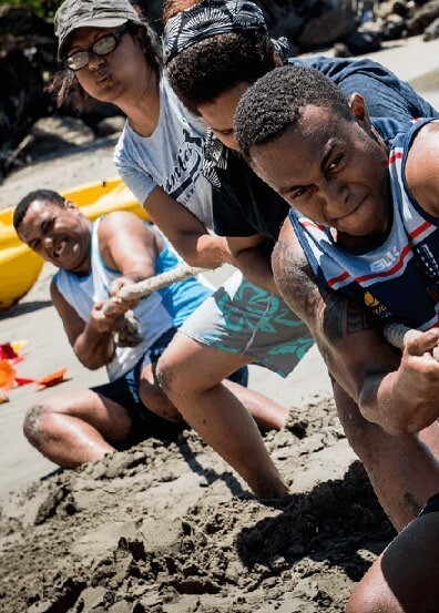 Sports team members straining fiercely in a tug-of-war game on a sandy beach for a team building exercise
