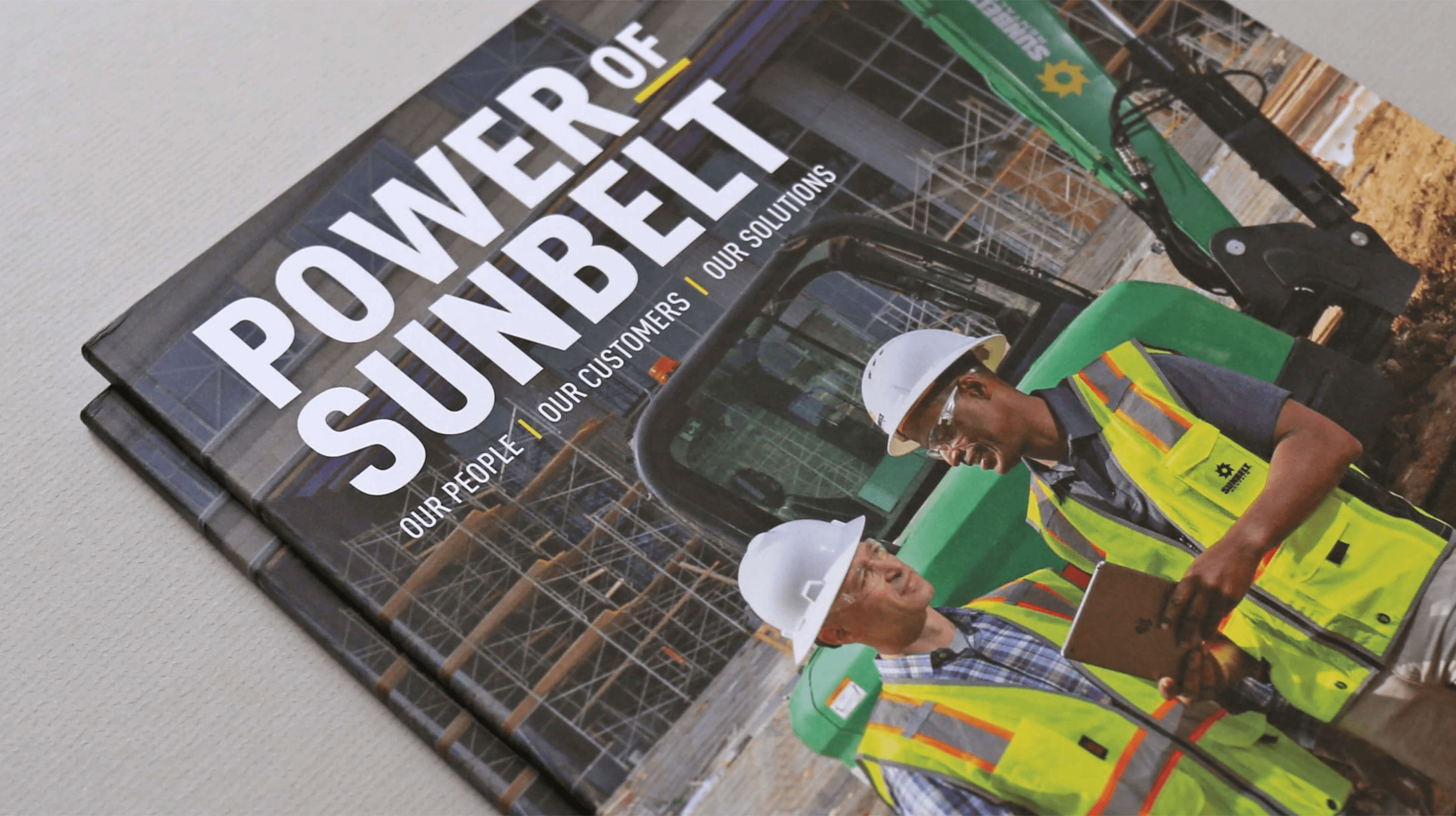 Front cover of the Sunbelt Publication featuring two employees in safety gear at a construction site, standing near a Sunbelt-branded bulldozer.