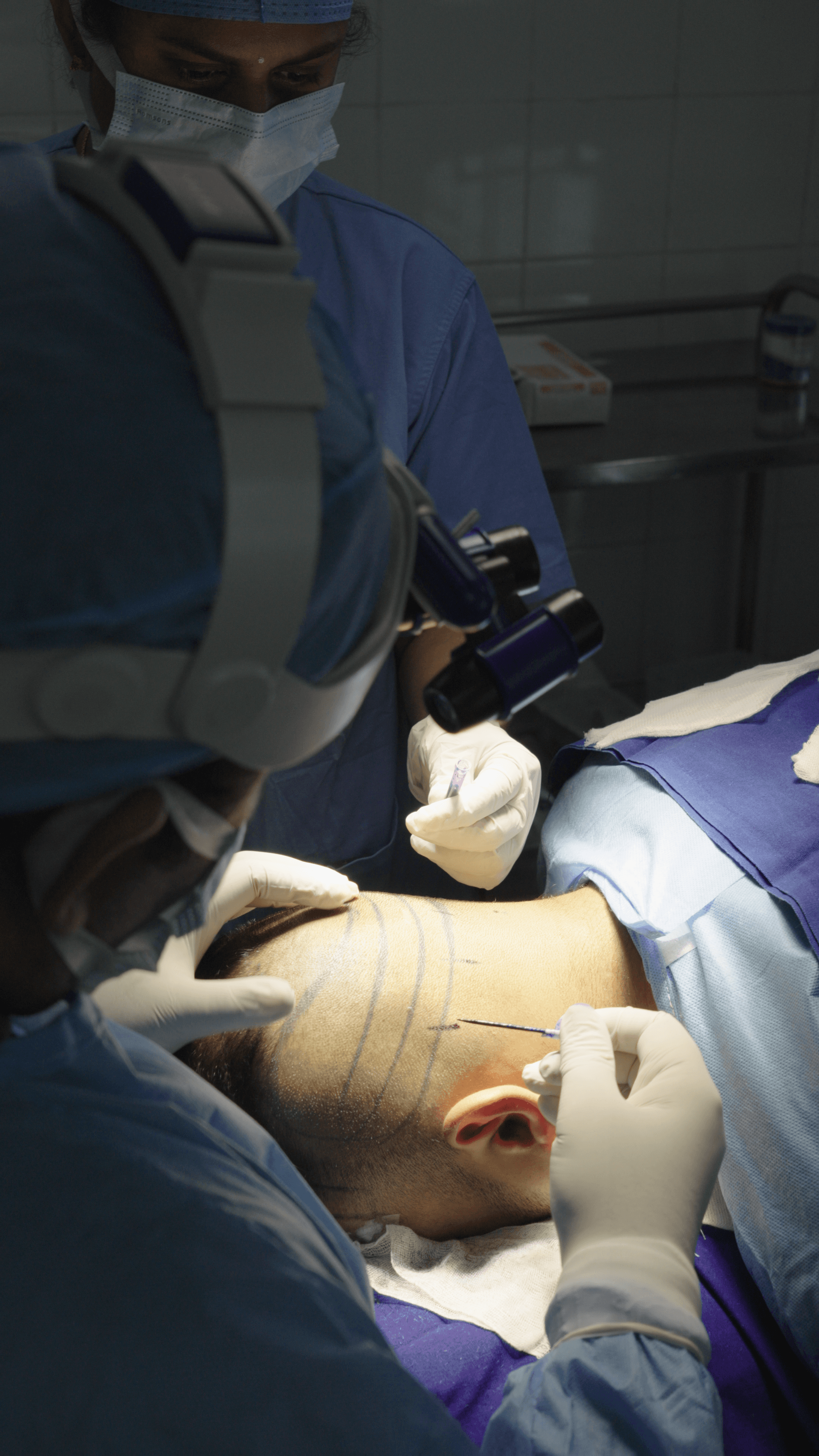 Healthcare worker in blue scrubs adjusting gloves in clinical setting with green curtains and equipment