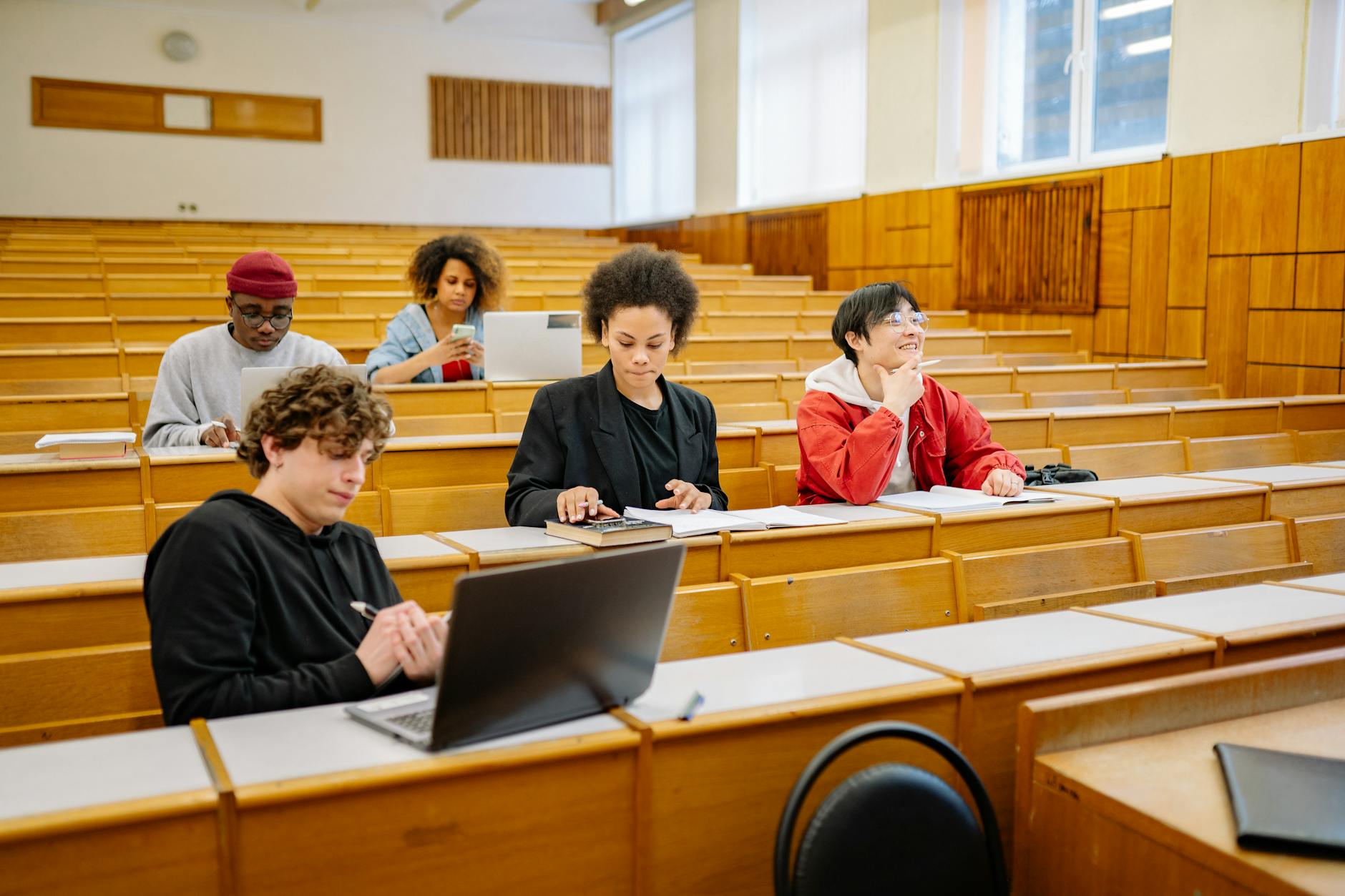 A young woman in a modern library using a tablet and headphones to conduct independent research for her thesis.