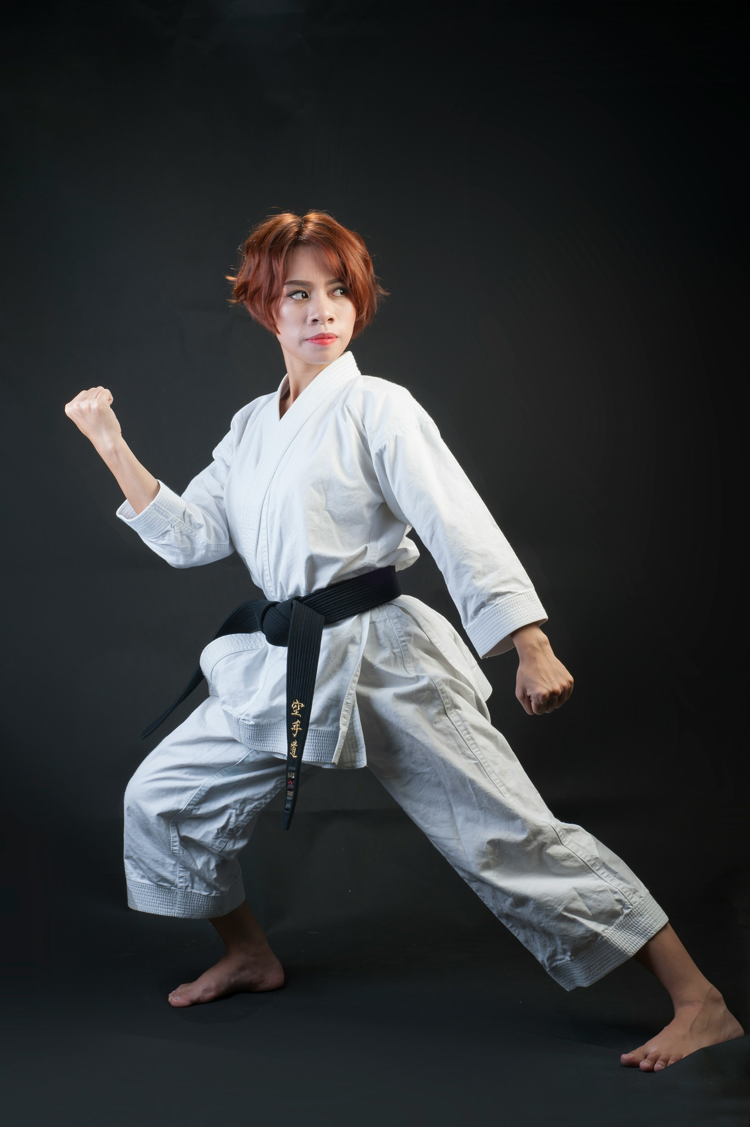 A karate black belt in a low stance against a dark background