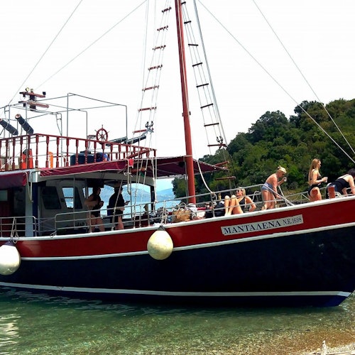 一艘紅黑色的船，旁邊有人在日光浴和放鬆，停泊在樹林覆蓋的海岸附近。