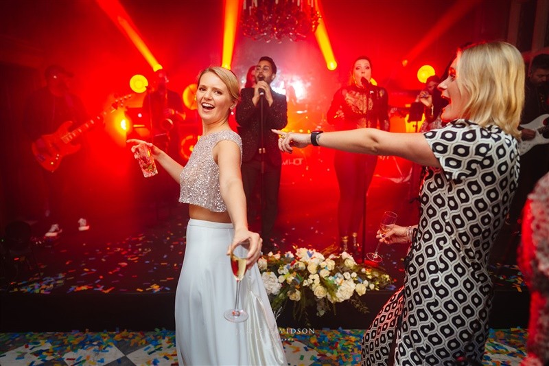 Maddy and wedding guests dancing under warm red stage lighting