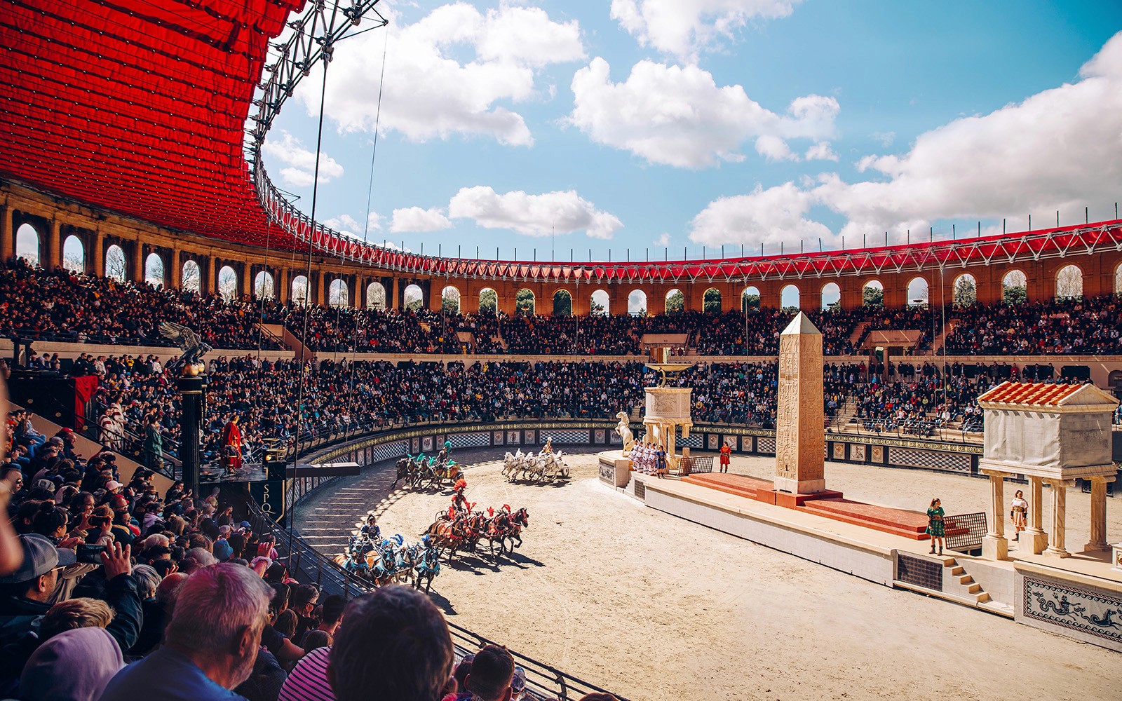 Chariot race in Puy du Fou arena with large audience and ancient Roman architecture.
