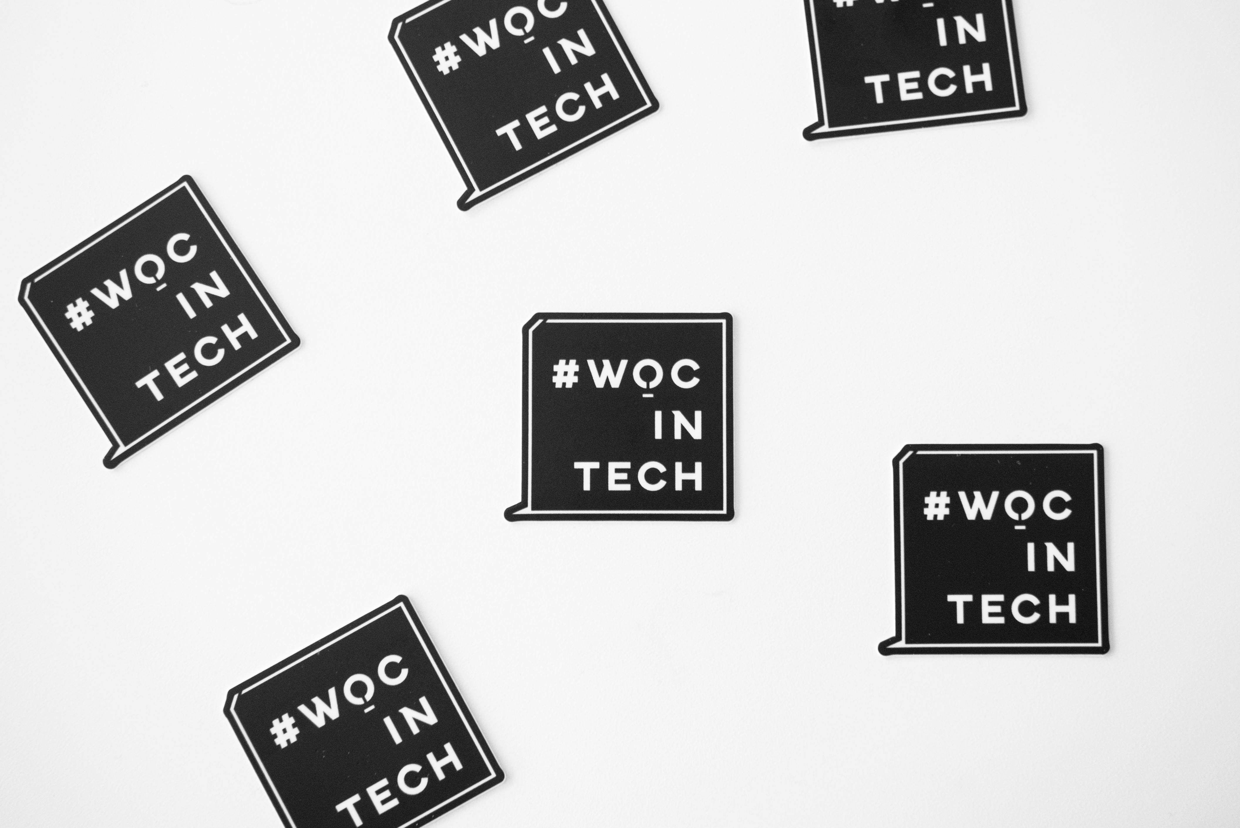 Several black square stickers with the text '#WOC IN TECH' scattered on a white background