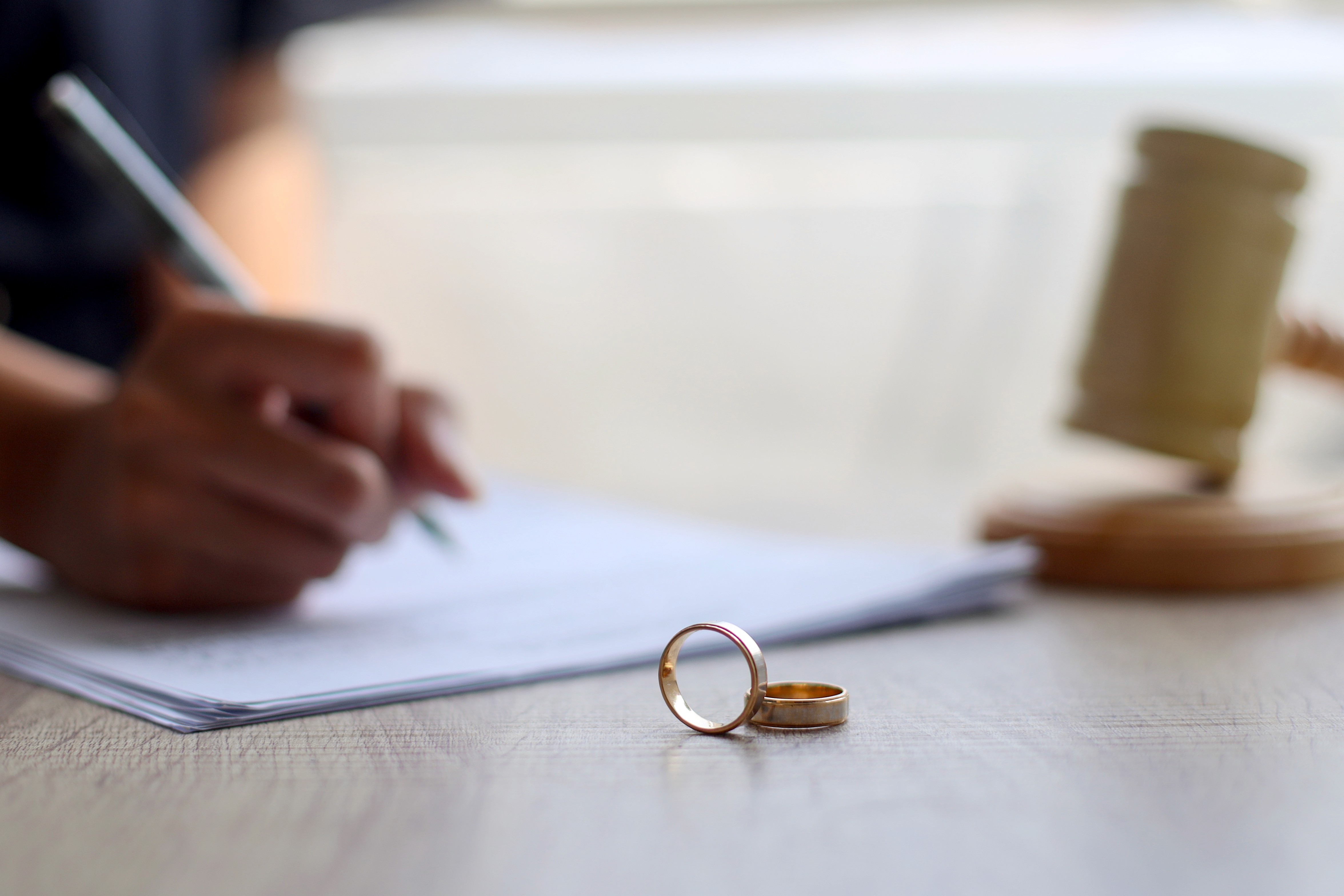 Person signing divorce documents with wedding rings on the table, representing the steps to prepare for divorce proceedings in Massachusetts with Lamb & Lamb, P.C.