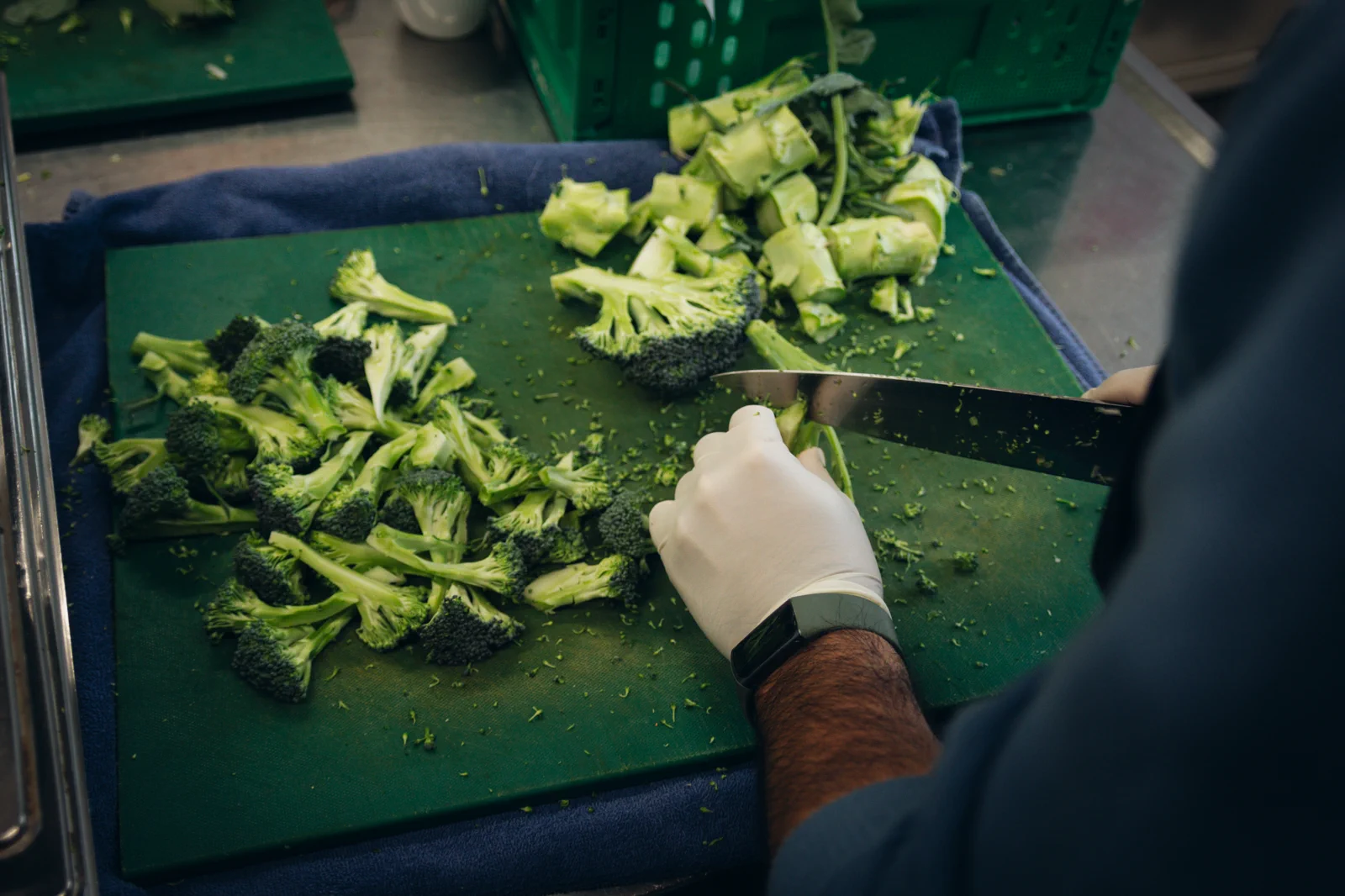 Hands chopping broccoli on a cutting board