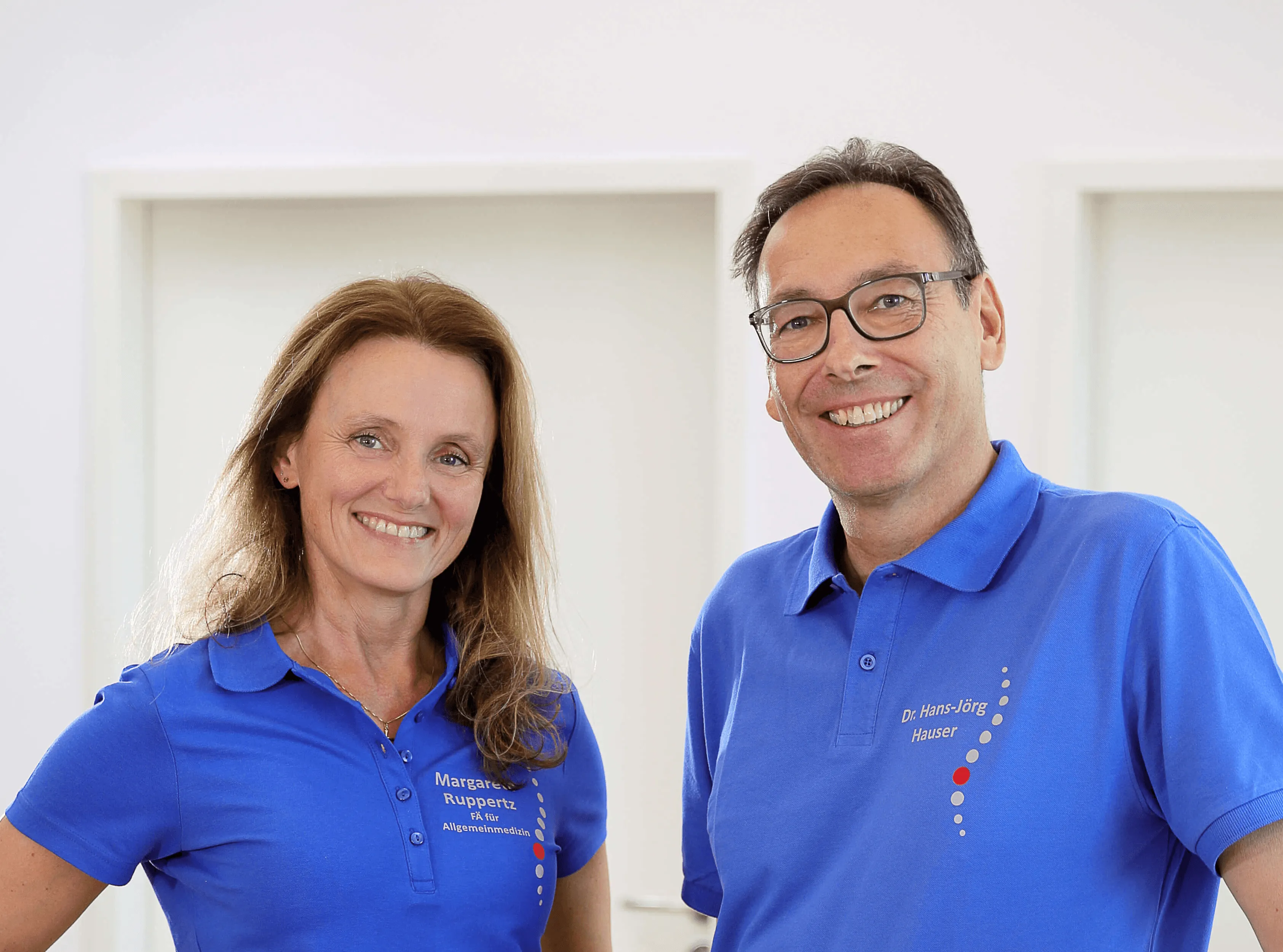 Two smiling individuals in blue shirts stand side by side against a light background.