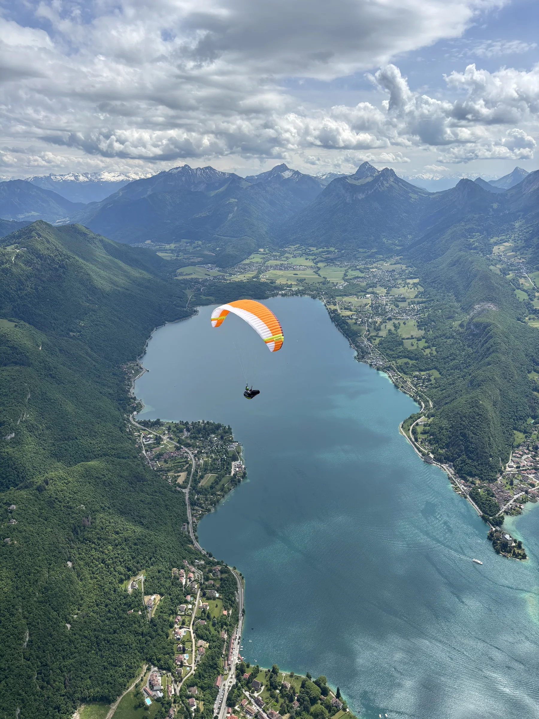 Orange paraglider flying above Lake Annecy