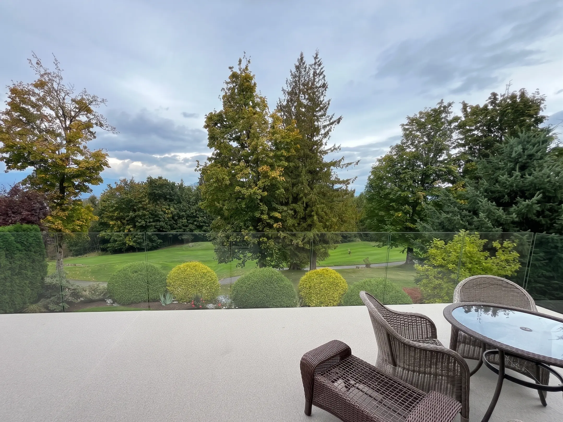 Frameless glass railing surrounding a residential patio with lawn and evergreen trees on a Vancouver Island property