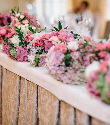 A row of colorful floral arrangements in shades of pink, white, and green on a wooden table.