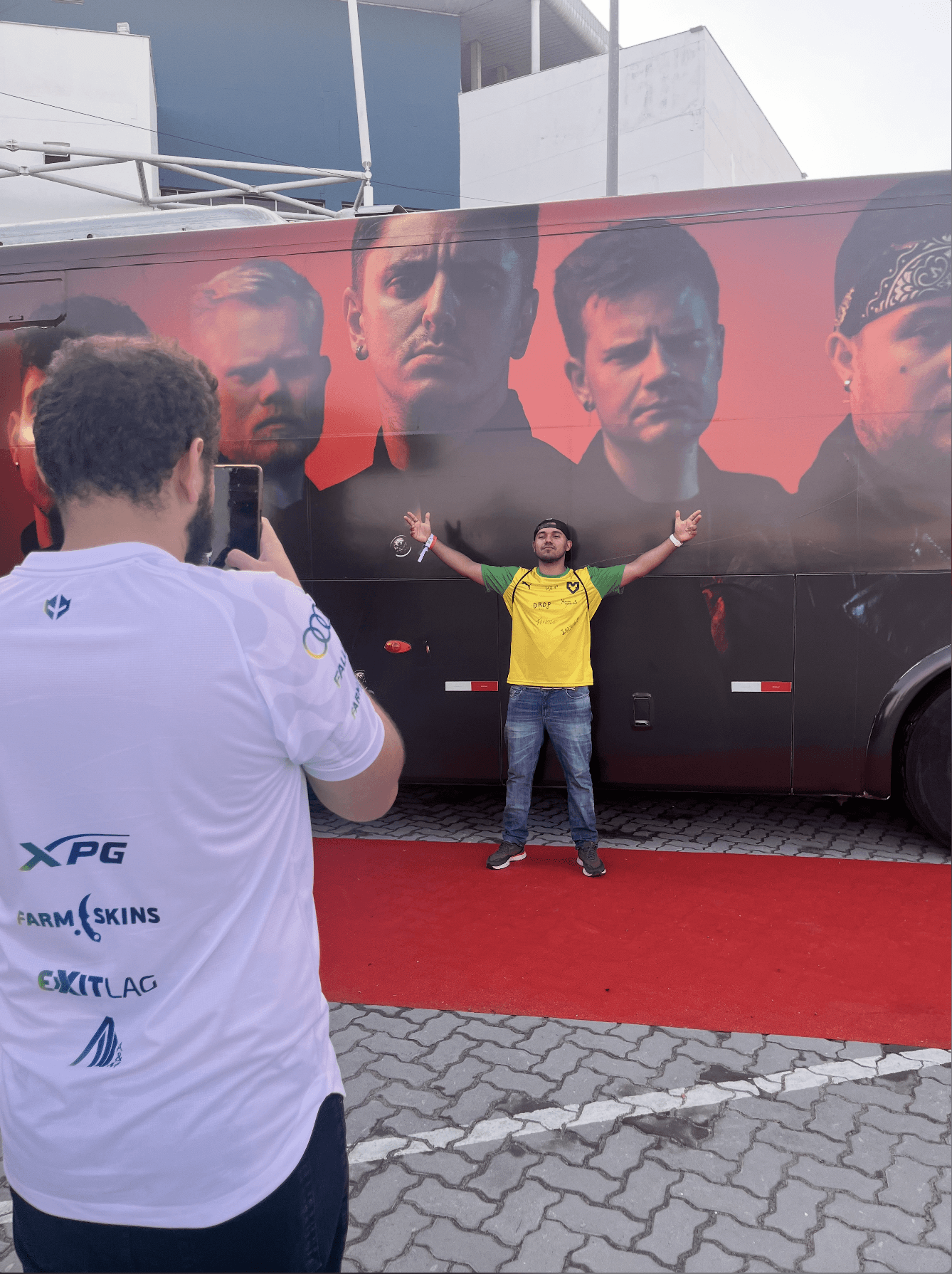 Visuel du projet Metality : Un homme portant un maillot blanc prend en photo un autre homme en maillot jaune et vert devant le bus de l'équipe Metality.