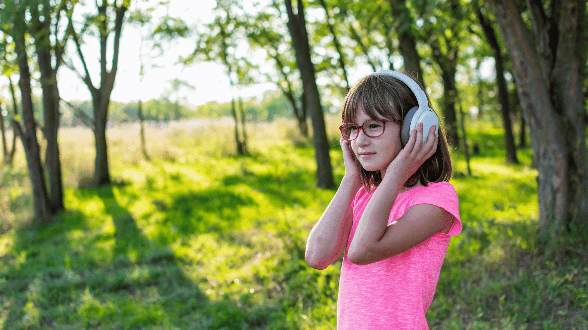 A young girl wearing a pink top and headphones, standing in the forest and listening to HushAway®’s Sound Sanctuary.