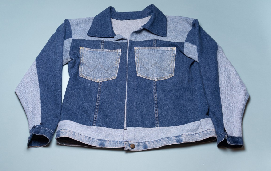 Flat lay of a blue patchwork denim jacket with contrasting panels and front pockets.