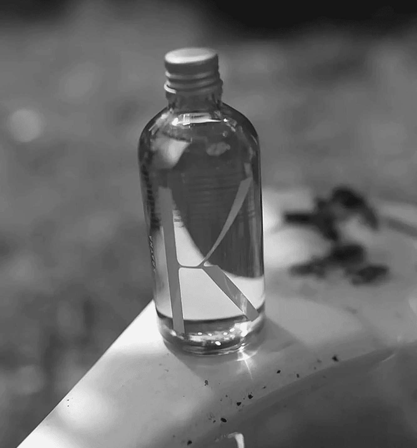 A transparent glass bottle with a large, frosted "K" logo reflects the natural sunlight. This bottle design emphasizes eco-friendly packaging and a "less is more" aesthetic developed by the Zurich design agency.