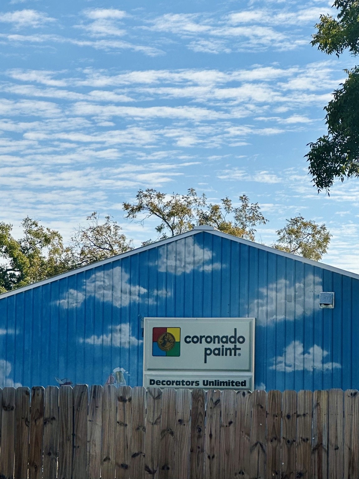 Painted white clouds on a blue Coronado Paint building beneath real clouds