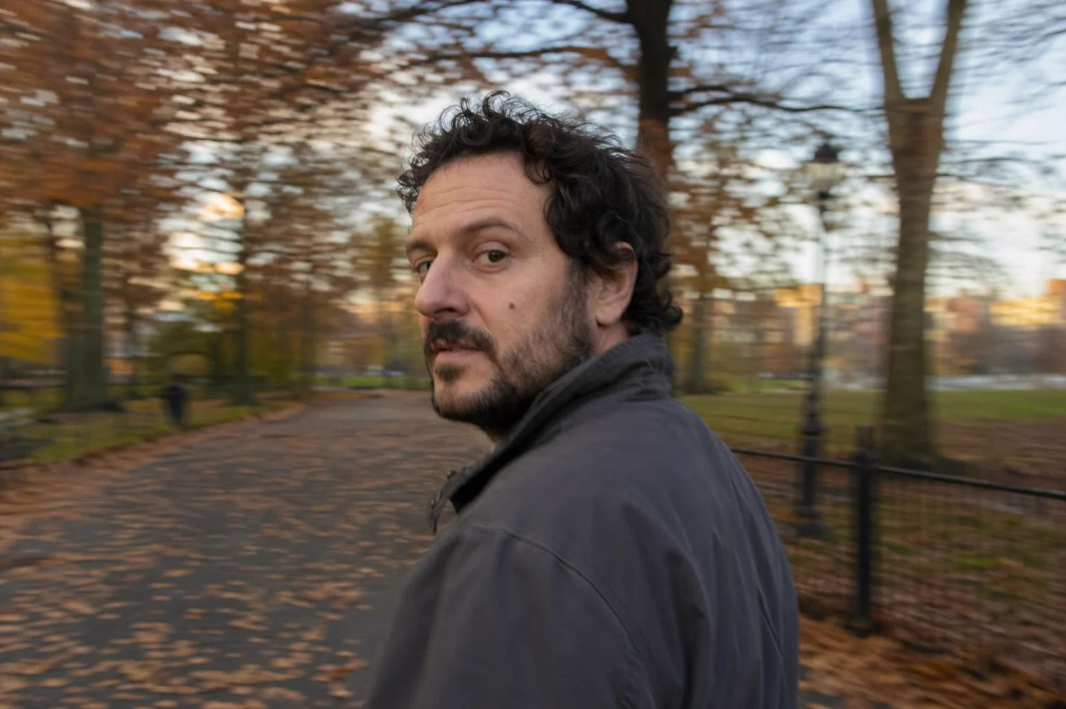 Man walking through autumn park looking back at camera.