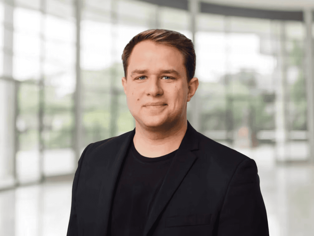 Enrico Bernardo, Geschäftsführer der hellomed Group GmbH, Portrait eines Mannes im schwarzen Sakko vor moderner Glasarchitektur.