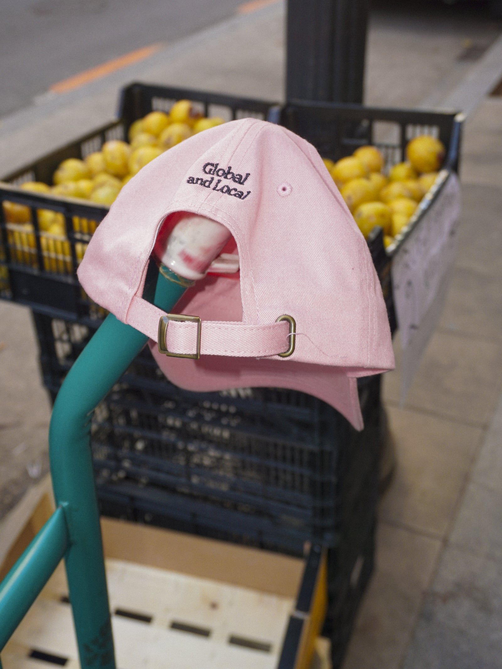 Pink cap with 'Global and Local' text on a shopping cart with lemons in the background.
