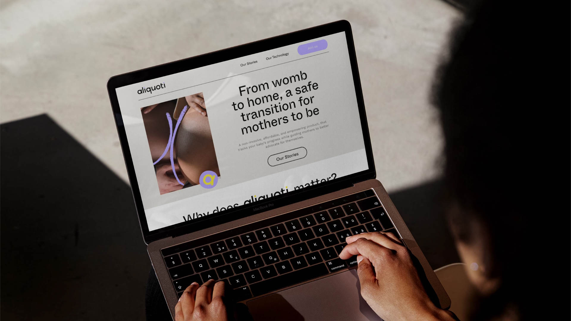 A person with dark hair is using a silver laptop. The screen displays the website aliquoti.com, which features a large image of a womb and text that reads: “From womb to home, a safe transition for mothers to be.” The website’s navigation bar includes “Our Stories,” “Our Technology,” and “Join Us.” The person’s hands are positioned on the keyboard as they interact with the laptop.