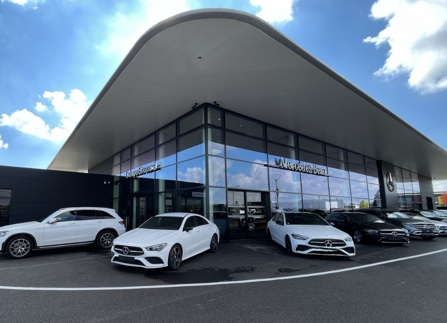 Façade vitrée d’un bâtiment industriel moderne avec auvent incliné et véhicules stationnés à l’avant.