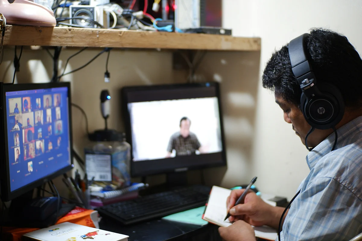 A learner wearing headphones and taking notes during a video lesson.