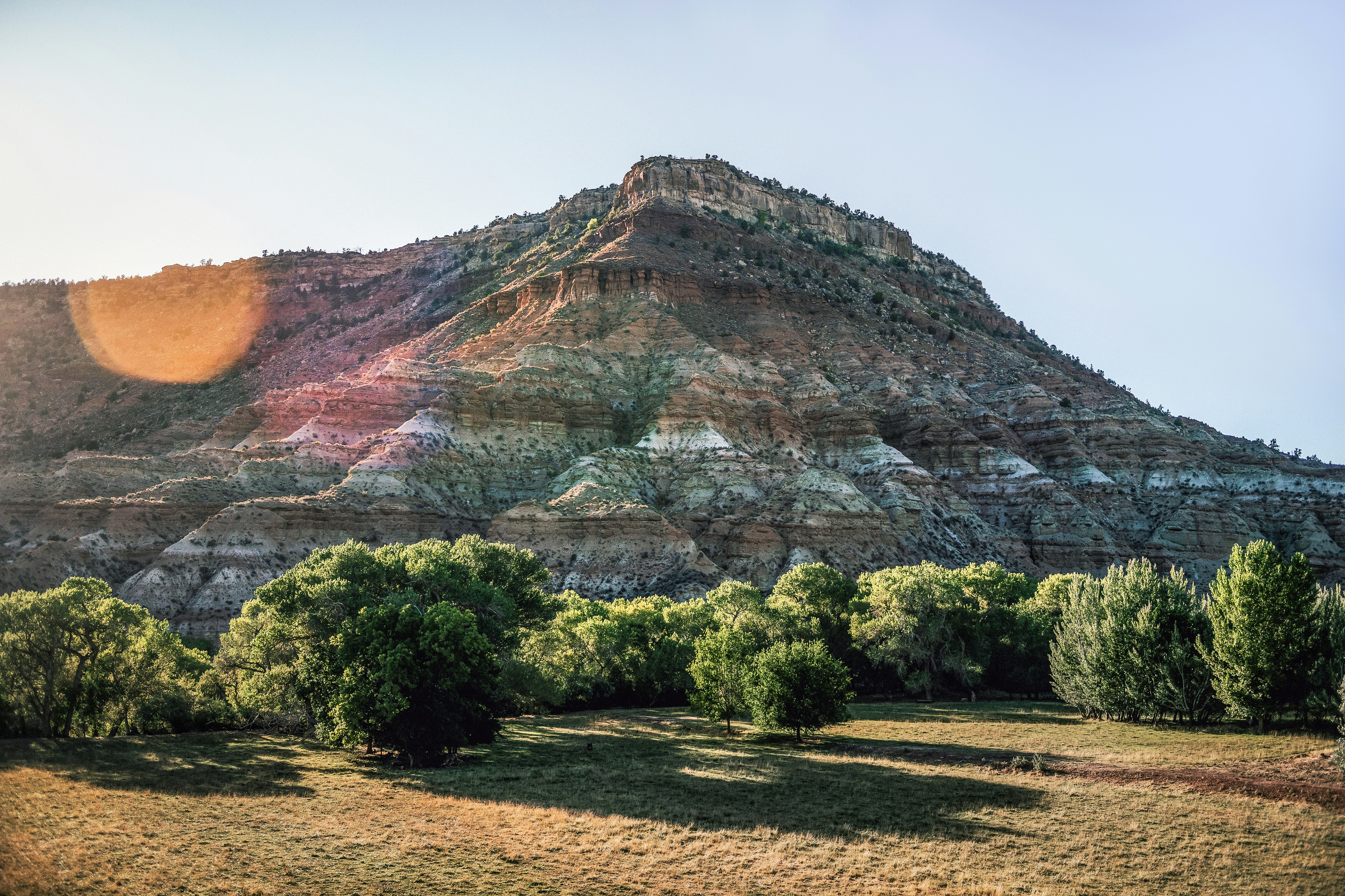 Layered mountain with trees in the foreground at sunset.
