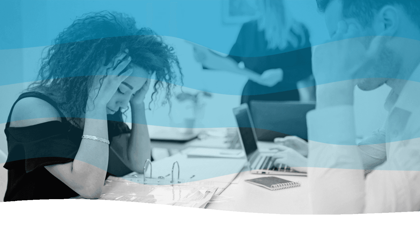 A woman sits at a desk with her head in her hands, appearing stressed, while a man works on a laptop nearby, embodying the theme of workplace stress and pressure.