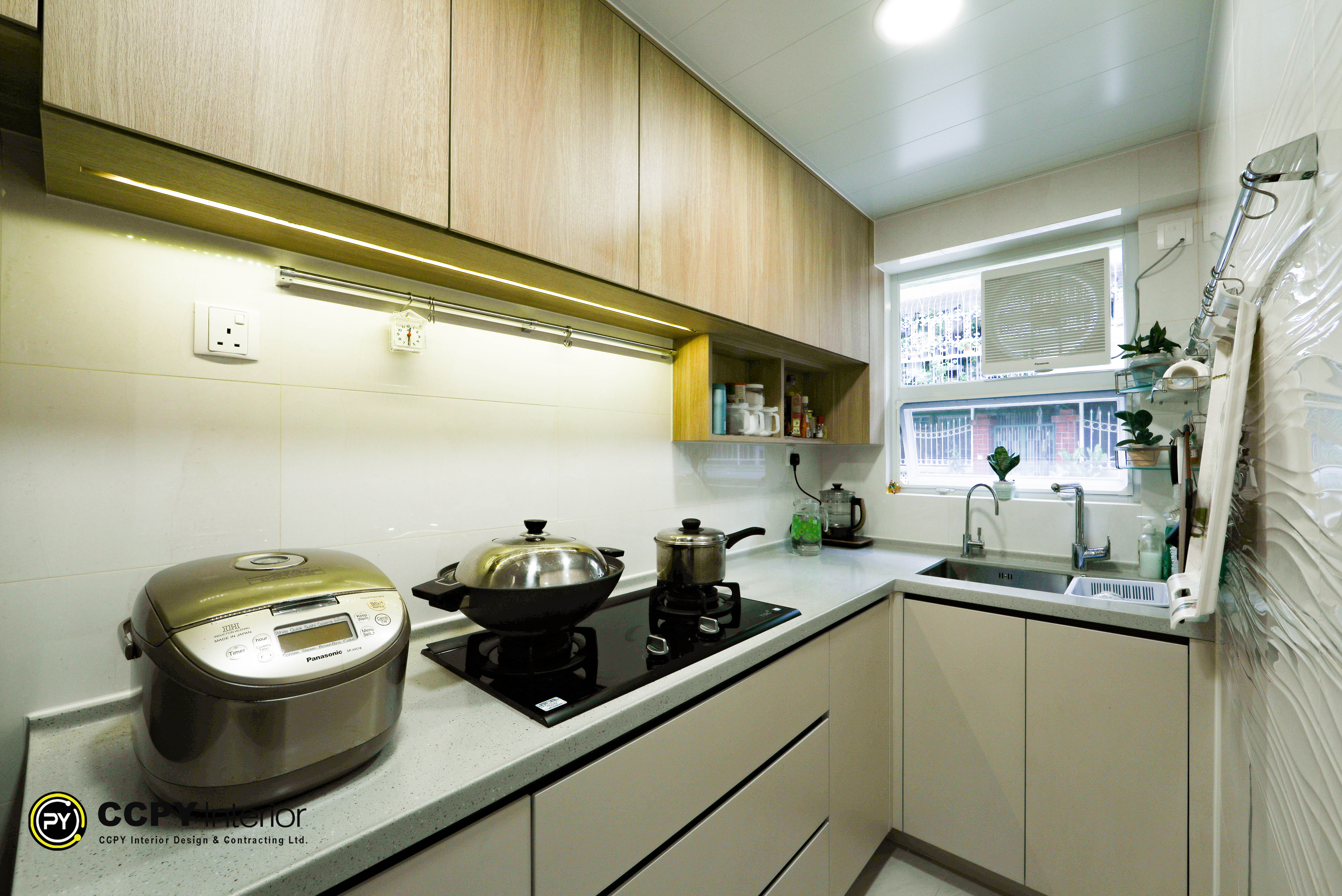Modern L-shaped kitchen interior design featuring light wood cabinets, under-cabinet lighting, and a neutral stone countertop by CCPY Interior Design."