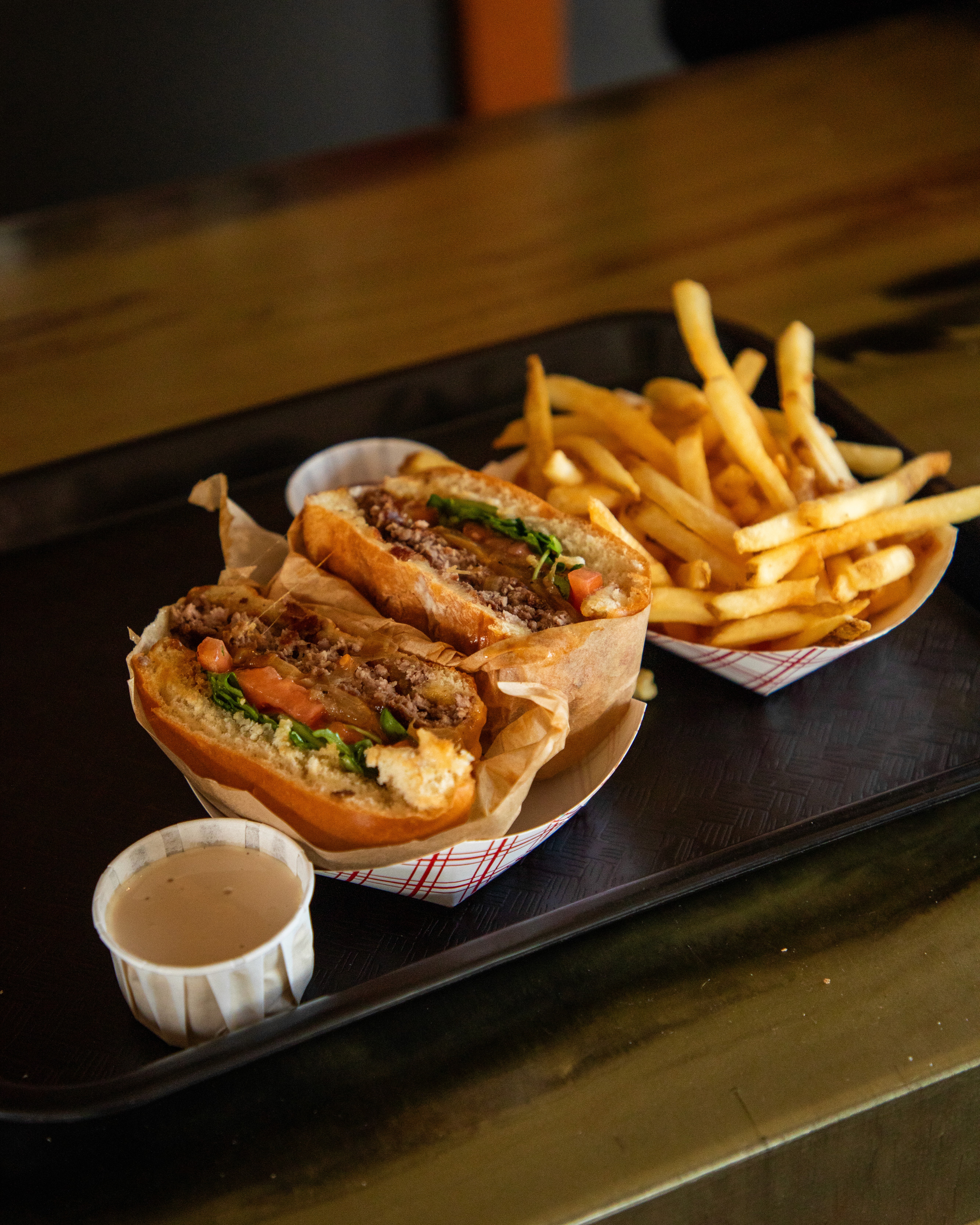 A rustic indoor scene featuring a table set for a meal, including two bowls of rice-based dishes topped with garnishes, an oil bottle, bread, a glass of juice, and milk bottles, all bathed in natural light streaming from a window.