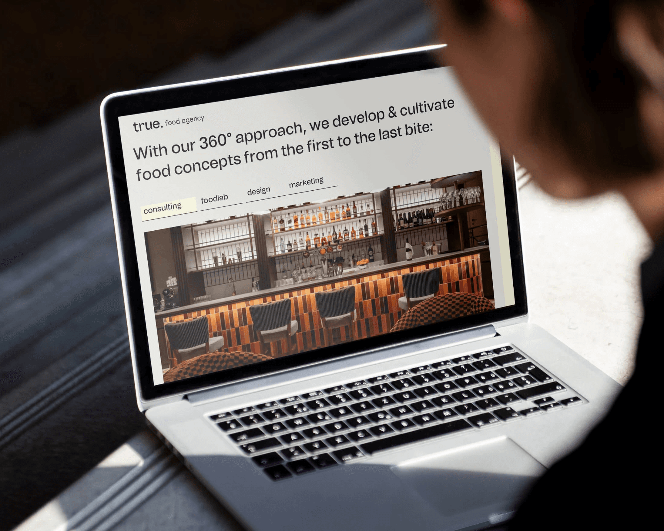 Laptop mockup showing True food agency website with restaurant interior and consulting tab