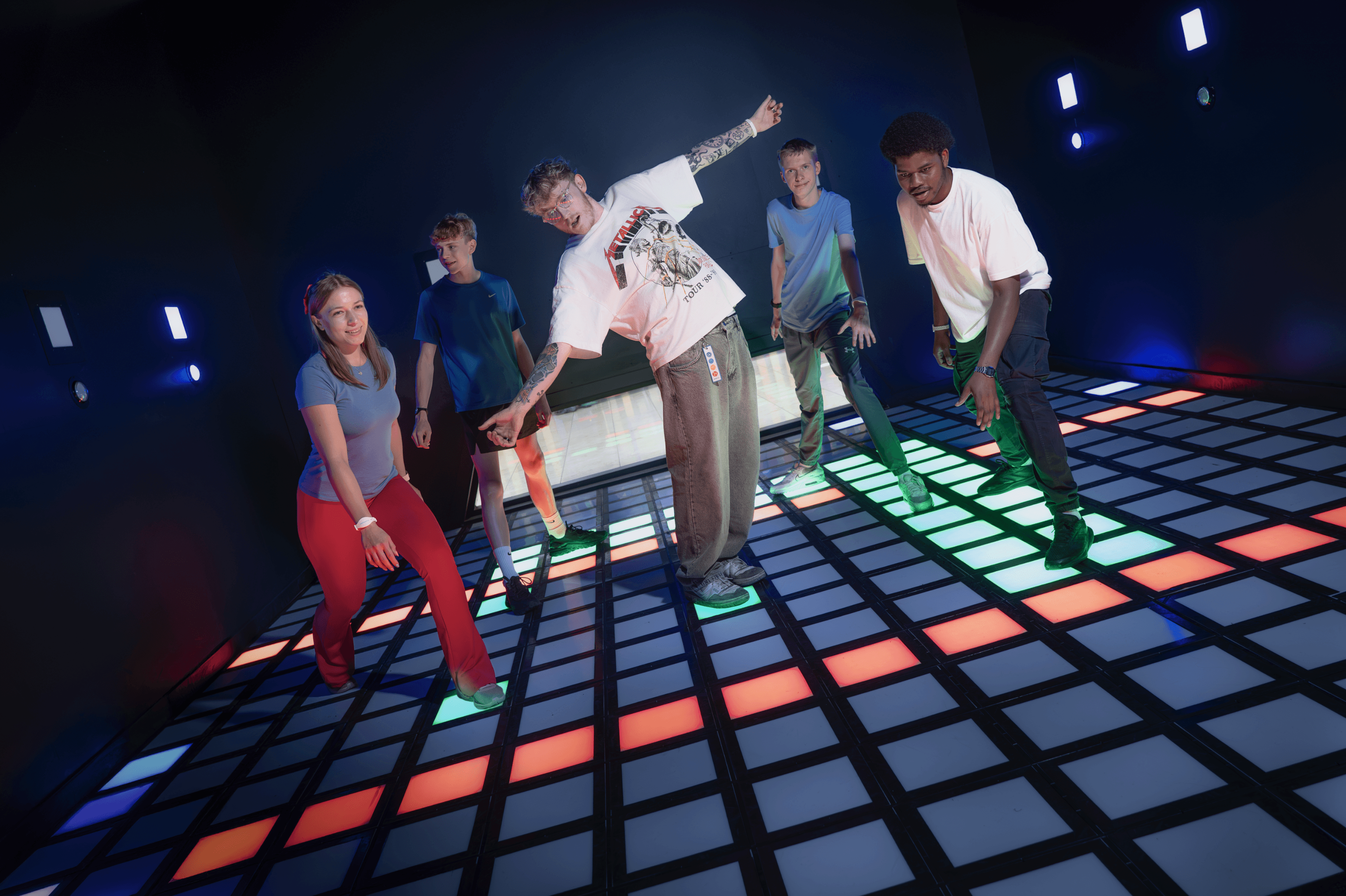 A low angle shot of a man with a beard leaning over a DJ mixer, other people are in the background.