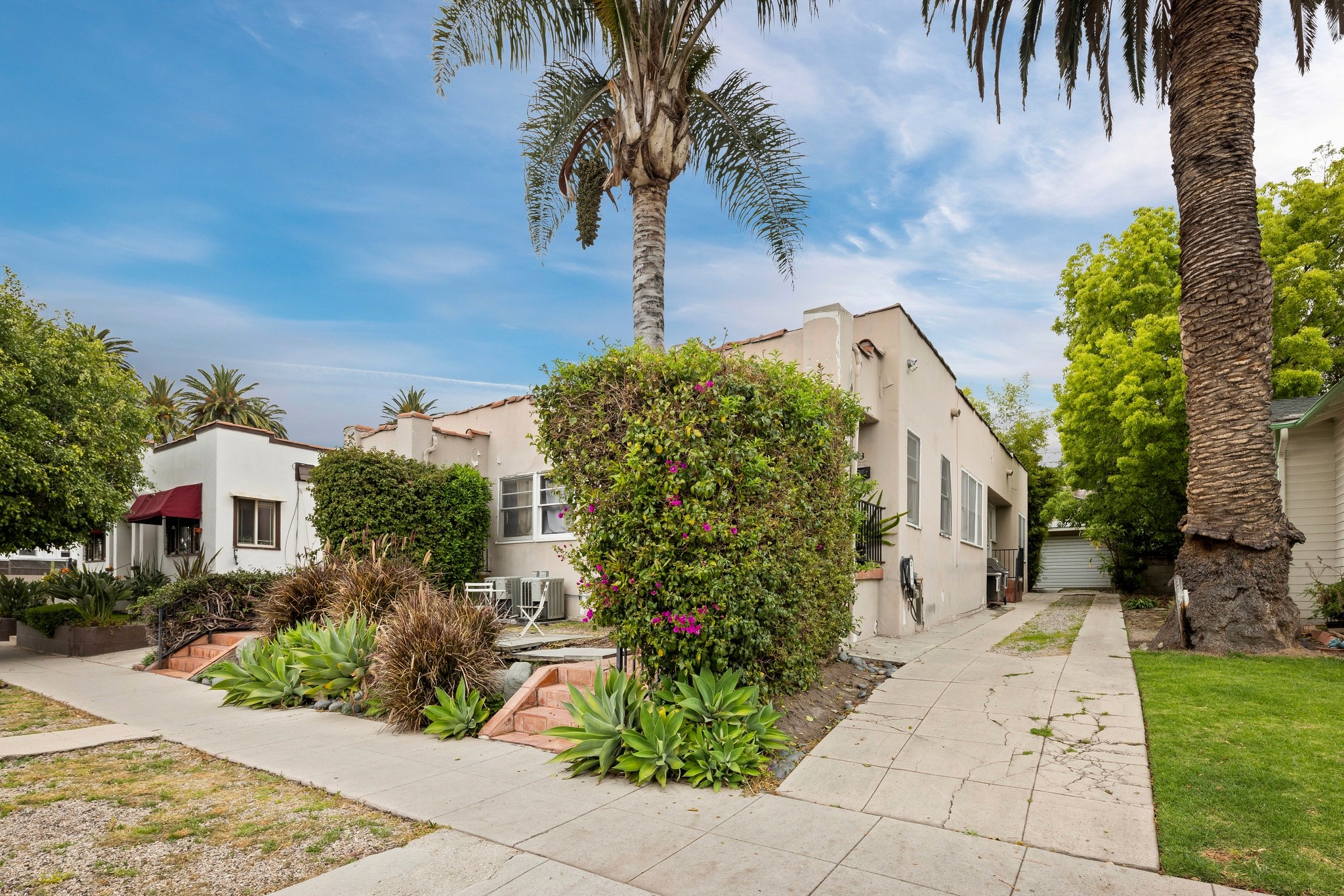 A sunny residential street near 4533 ambrose ave, lined with shrubs, leading to a house with palm trees and a clear blue sky.